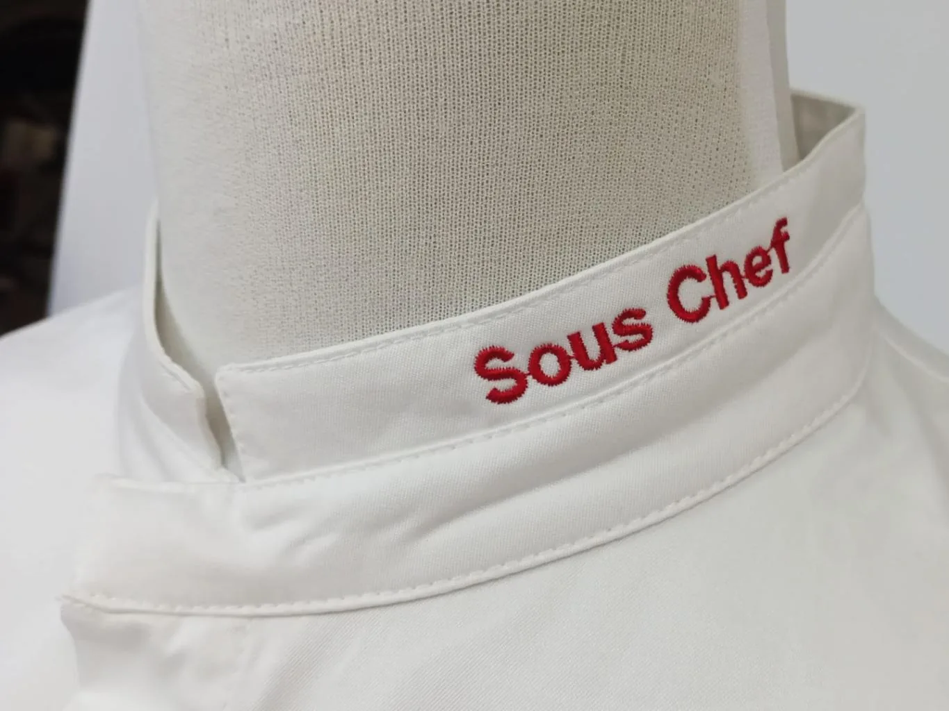 Texto bordado en rojo en el cuello de una chaqueta blanca